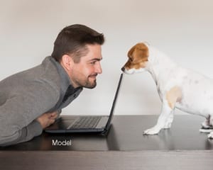 a man staring at a dog behind a laptop