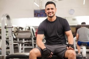 Athletic adult male model sitting on a workout bench inside a gym