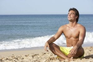 Adult male model in bathing suit sitting on the sands of a beach in a relaxed state