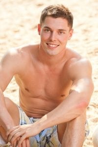 Young adult male model shirtless with an athletic build sitting on the beach