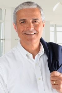 Headshot of a middle aged male model in a white button shirt holding his suit jacket over his shoulders