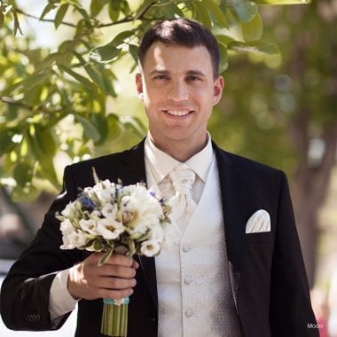Headshot of a groom in a tuxedo holding up a bouquet of flowers
