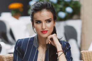 Woman in a nice blue suit with red lipstick sitting in a chair.