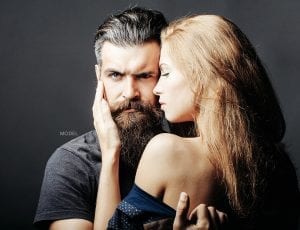A male model with a full set of hair and a full beard being held by a female model