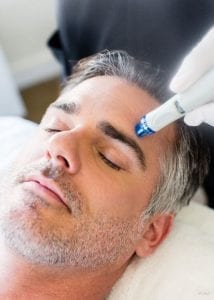 Headshot of middle aged male model laying in spa bed receiving hydrafacial treatment in his forehead
