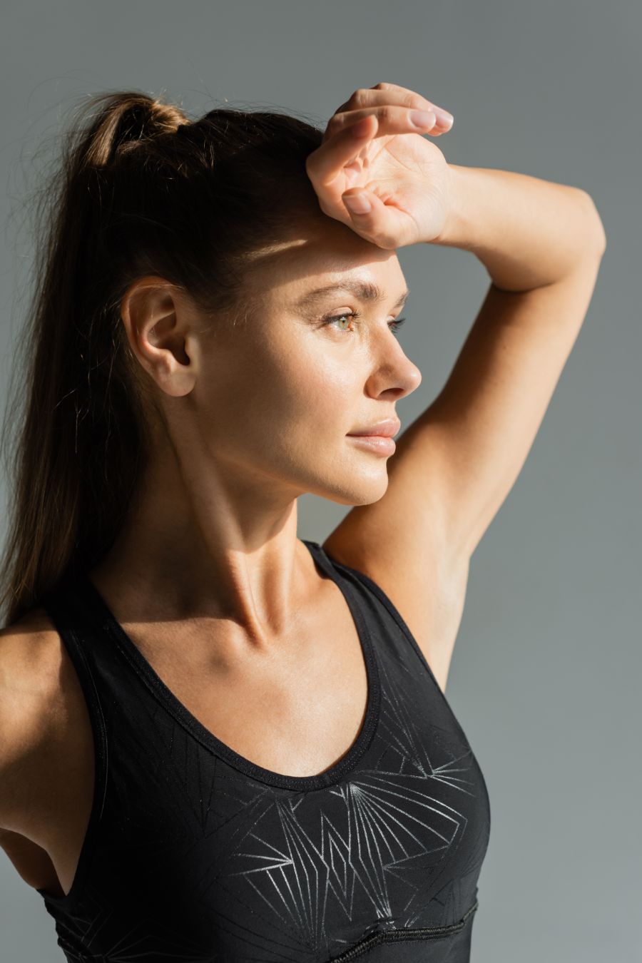 woman wearing a black sports bra, a high ponytail, and the back of her hand raised to her forehead